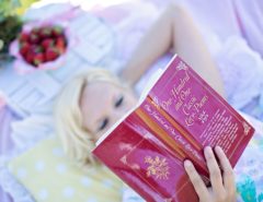 Eine Person mit blonden Haaren liegt auf einer Picknickdecke und liest ein Buch mit dem Titel "One Hundred and One Classic Love Poems".