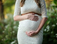 Eine schwangere Frau in einem weißen Kleid greift auf ihren Bauch.